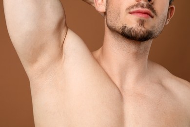 Photo of Young man showing smooth armpit after epilation procedure on brown background