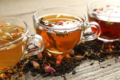 Photo of Different herbal teas and dry leaves on wooden table, closeup