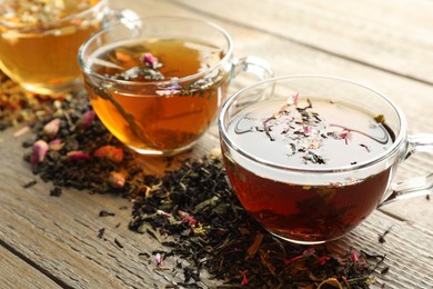 Photo of Different herbal teas and dry leaves on wooden table, closeup