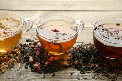 Photo of Different herbal teas and dry leaves on wooden table, closeup
