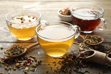 Photo of Different herbal teas and dry leaves on wooden table, closeup