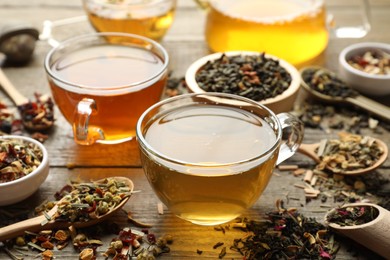 Photo of Different herbal teas and dry leaves on wooden table, closeup