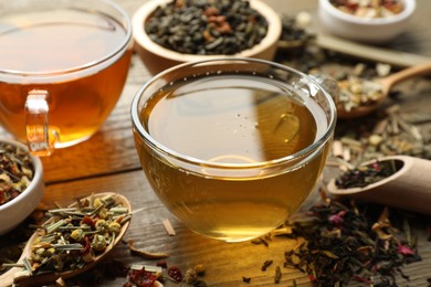 Photo of Different herbal teas and dry leaves on wooden table, closeup