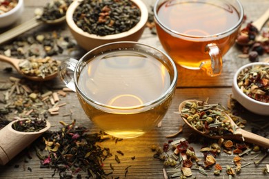 Photo of Different herbal teas and dry leaves on wooden table, closeup