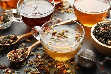 Photo of Different herbal teas and dry leaves on black table, closeup