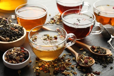 Photo of Different herbal teas and dry leaves on black table, closeup