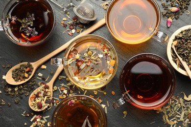 Photo of Different herbal teas and dry leaves on black table, flat lay