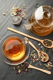 Photo of Delicious herbal tea and dry leaves on black table, flat lay