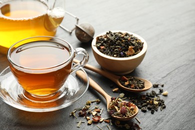 Photo of Delicious herbal tea and dry leaves on black table, closeup