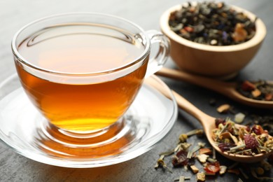 Photo of Delicious herbal tea and dry leaves on black table, closeup