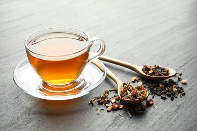 Photo of Delicious herbal tea and dry leaves on black table, closeup