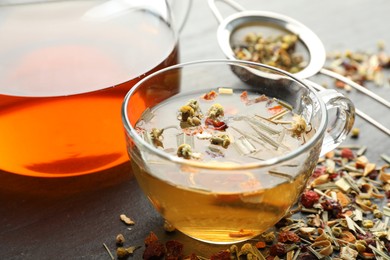 Photo of Delicious herbal tea and dry leaves on black table, closeup