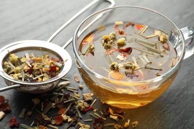 Photo of Delicious herbal tea and dry leaves on black table, closeup