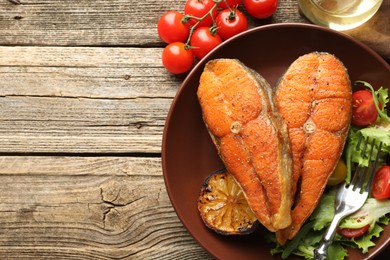 Photo of Seafood. Tasty salmon steaks served with salad and lemon on wooden table, flat lay. Space for text