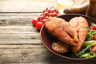 Photo of Seafood. Tasty salmon steaks served with salad and lemon on wooden table, closeup. Space for text