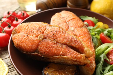 Photo of Seafood. Tasty salmon steaks served with salad on wooden table, closeup