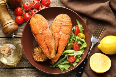 Photo of Seafood. Tasty salmon steaks served with salad and lemon on wooden table, flat lay