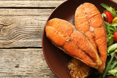 Photo of Seafood. Tasty salmon steaks served with salad and lemon on wooden table, top view. Space for text
