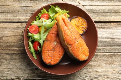 Photo of Seafood. Tasty salmon steaks served with salad and lemon on wooden table, top view