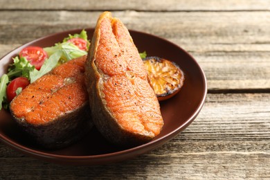 Photo of Seafood. Tasty salmon steaks served with salad and lemon on wooden table, closeup. Space for text