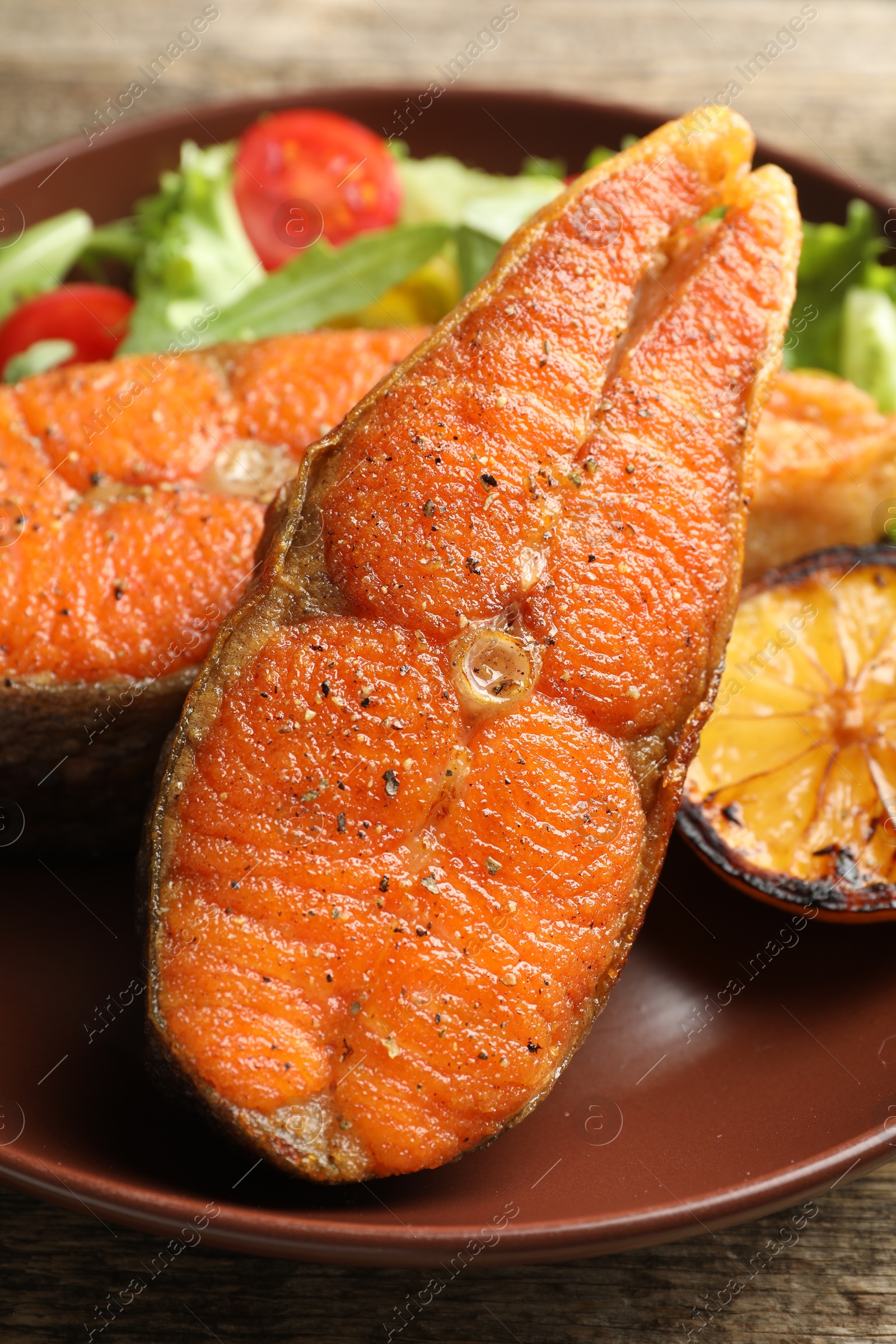 Seafood. Tasty salmon steaks served with salad and lemon on wooden table, closeup Photo of Seafood. Tasty salmon steaks served with salad and lemon on wooden table, closeup
