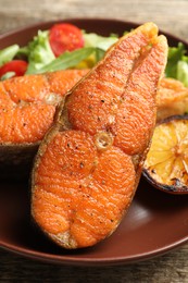 Photo of Seafood. Tasty salmon steaks served with salad and lemon on wooden table, closeup