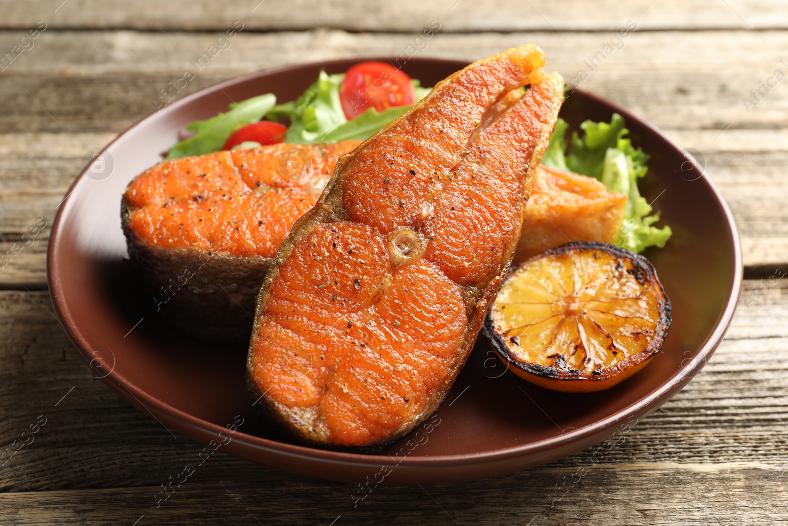 Seafood. Tasty salmon steaks served with salad and lemon on wooden table, closeup Photo of Seafood. Tasty salmon steaks served with salad and lemon on wooden table, closeup