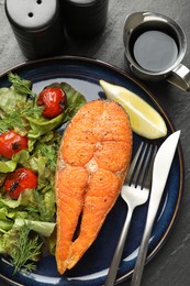 Photo of Seafood. Tasty salmon steak served with salad and lemon on black table, flat lay
