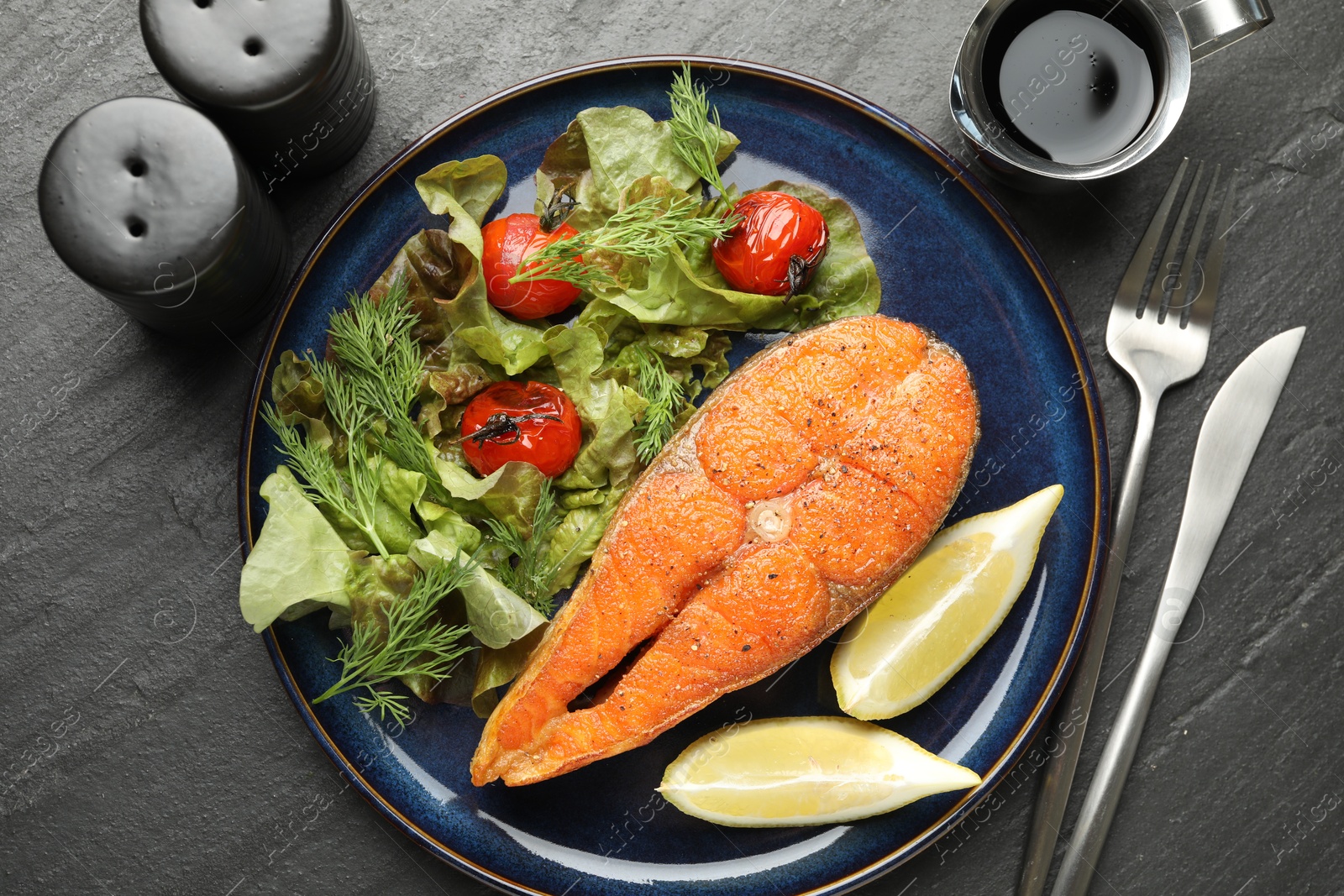 Seafood. Tasty salmon steak served with salad and lemon on black table, flat lay Photo of Seafood. Tasty salmon steak served with salad and lemon on black table, flat lay