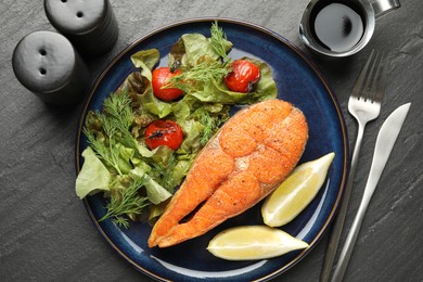 Photo of Seafood. Tasty salmon steak served with salad and lemon on black table, flat lay