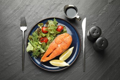 Photo of Seafood. Tasty salmon steak served with salad and lemon on black table, flat lay
