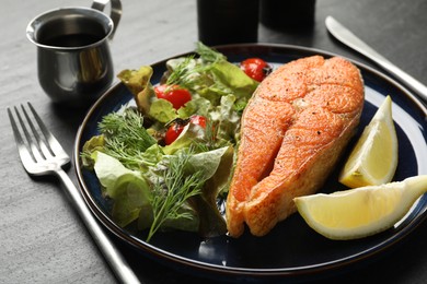 Photo of Seafood. Tasty salmon steak served with salad and lemon on black table, closeup