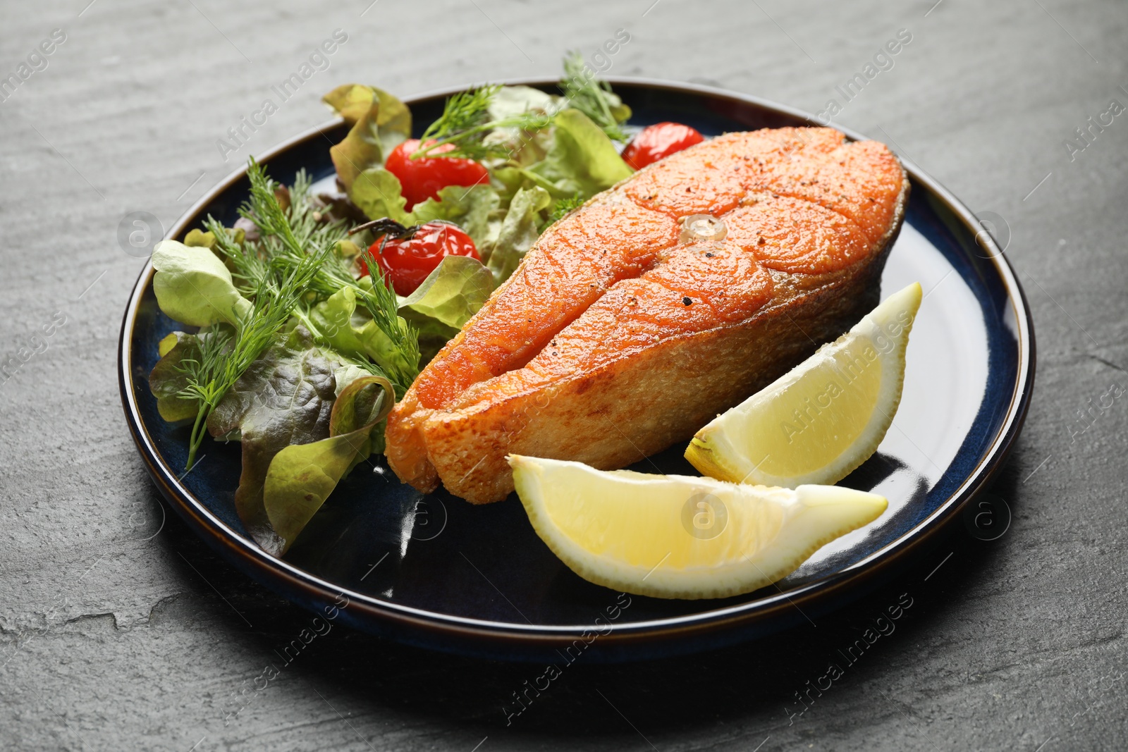 Seafood. Tasty salmon steak served with salad and lemon on black table, closeup Photo of Seafood. Tasty salmon steak served with salad and lemon on black table, closeup