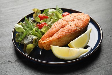 Photo of Seafood. Tasty salmon steak served with salad and lemon on black table, closeup