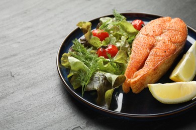 Photo of Seafood. Tasty salmon steak served with salad and lemon on black table, closeup. Space for text