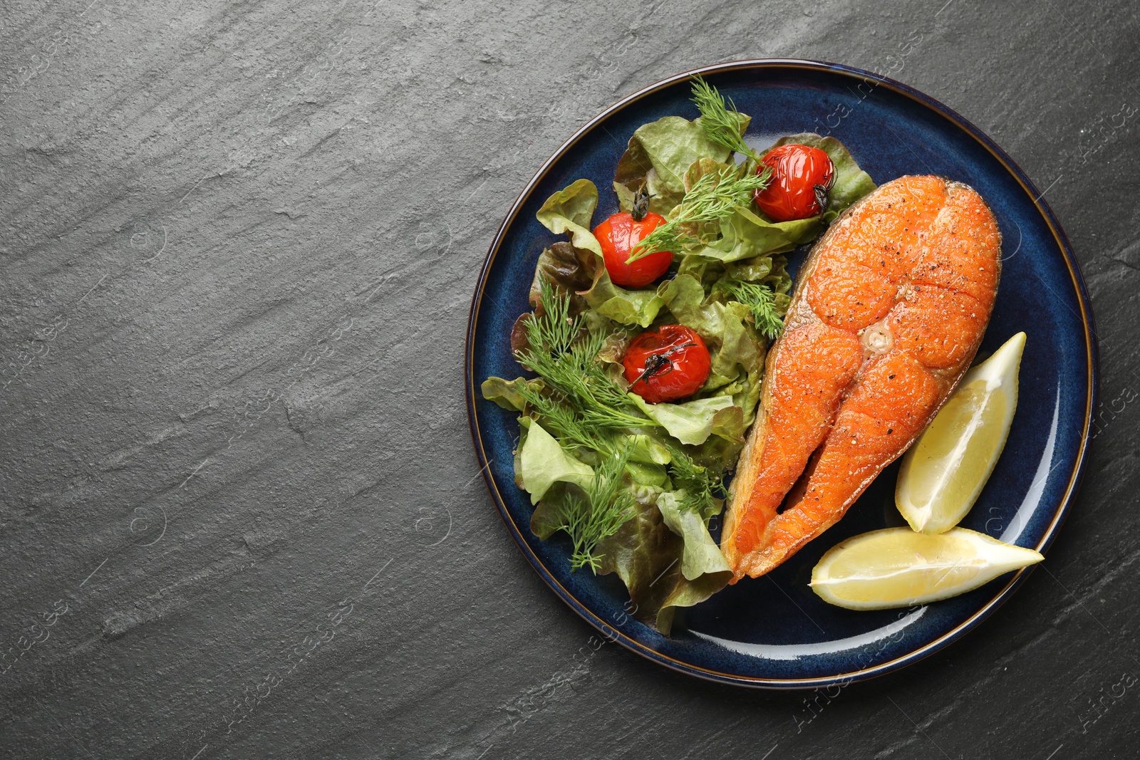 Seafood. Tasty salmon steak served with salad and lemon on black table, top view. Space for text Photo of Seafood. Tasty salmon steak served with salad and lemon on black table, top view. Space for text