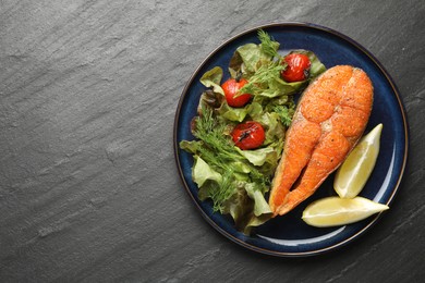 Photo of Seafood. Tasty salmon steak served with salad and lemon on black table, top view. Space for text