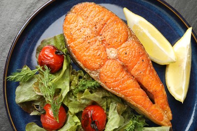 Photo of Seafood. Tasty salmon steak served with salad and lemon on black table, top view