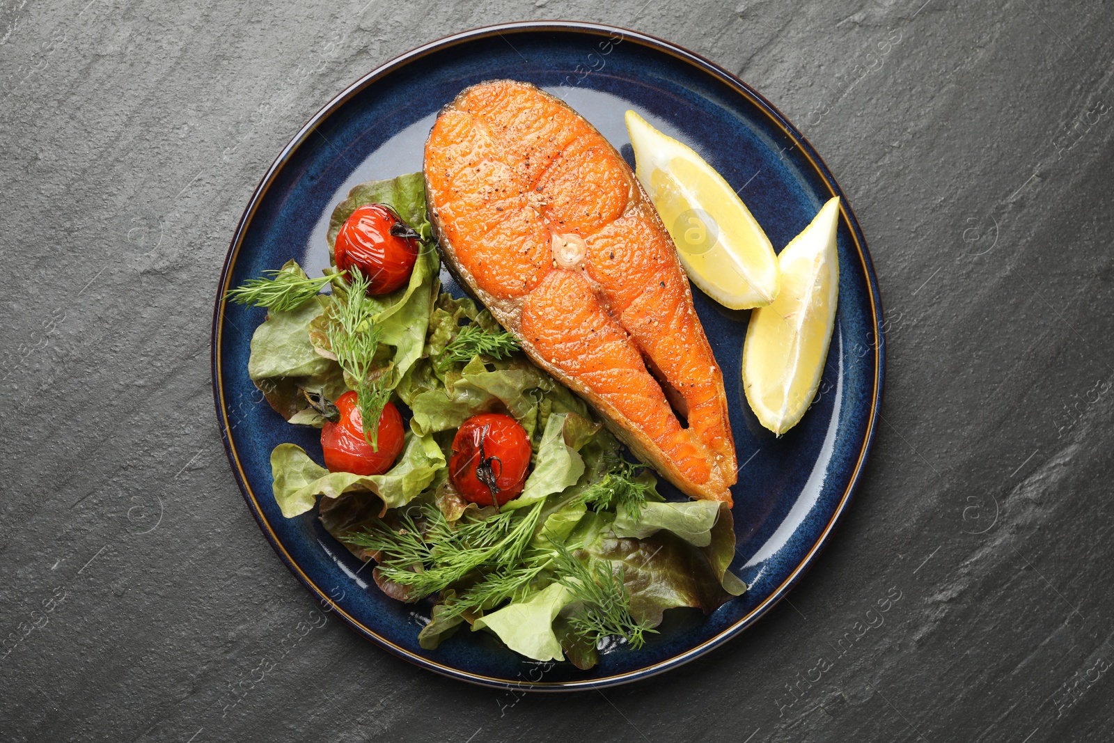 Seafood. Tasty salmon steak served with salad and lemon on black table, top view Photo of Seafood. Tasty salmon steak served with salad and lemon on black table, top view