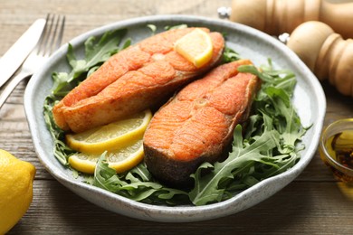 Photo of Seafood. Tasty salmon steaks served with arugula and lemon on wooden table, closeup
