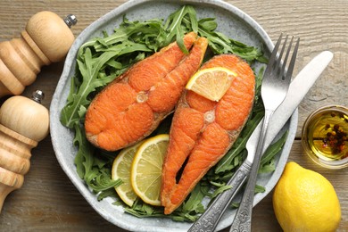 Photo of Seafood. Tasty salmon steaks served with arugula and lemon on wooden table, flat lay