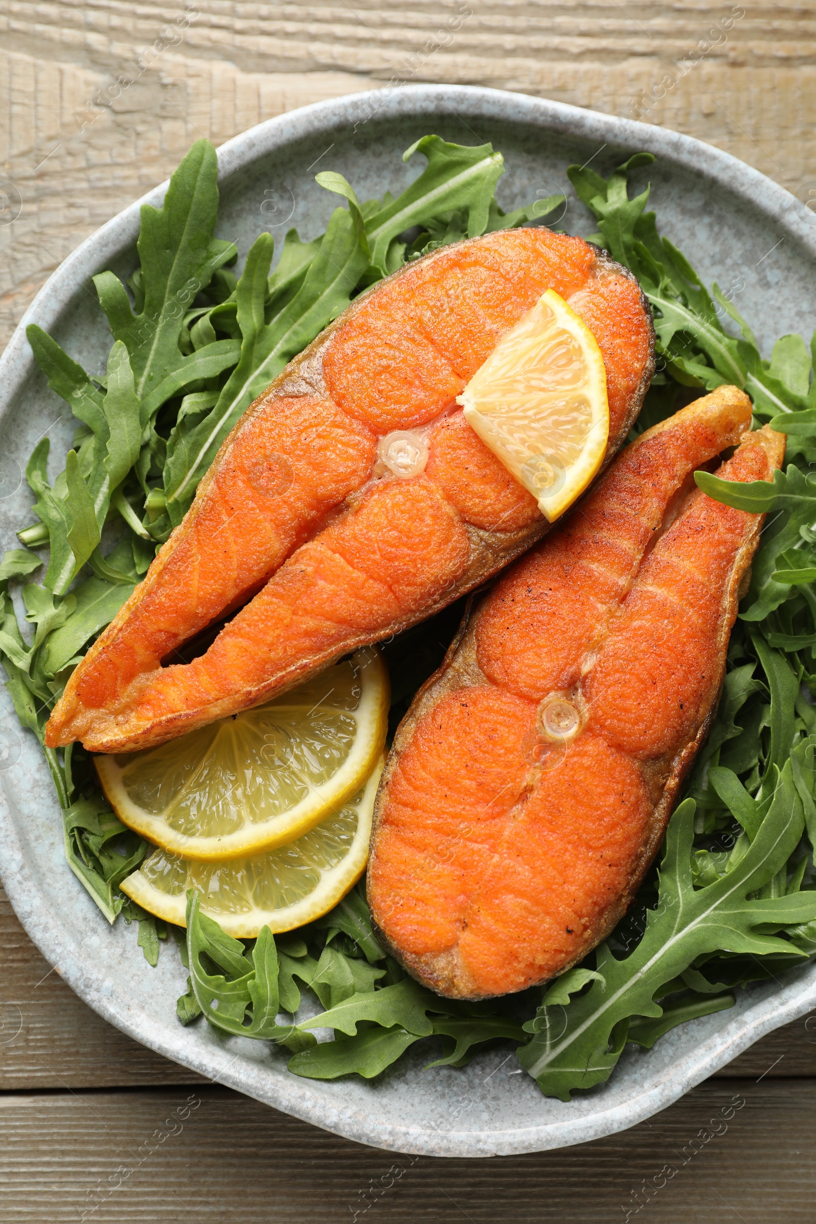 Seafood. Tasty salmon steaks, arugula and lemon on wooden table, top view Photo of Seafood. Tasty salmon steaks, arugula and lemon on wooden table, top view