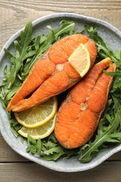 Photo of Seafood. Tasty salmon steaks, arugula and lemon on wooden table, top view