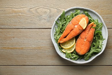 Photo of Seafood. Tasty salmon steaks served with arugula and lemon on wooden table, top view. Space for text