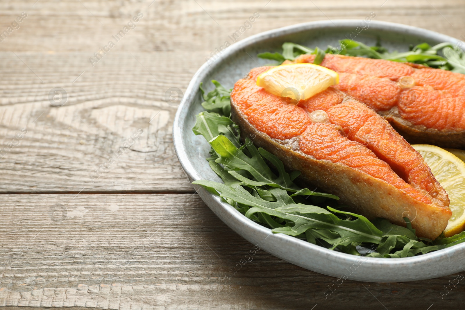 Seafood. Tasty salmon steaks, arugula and lemon on wooden table, closeup. Space for text Photo of Seafood. Tasty salmon steaks, arugula and lemon on wooden table, closeup. Space for text
