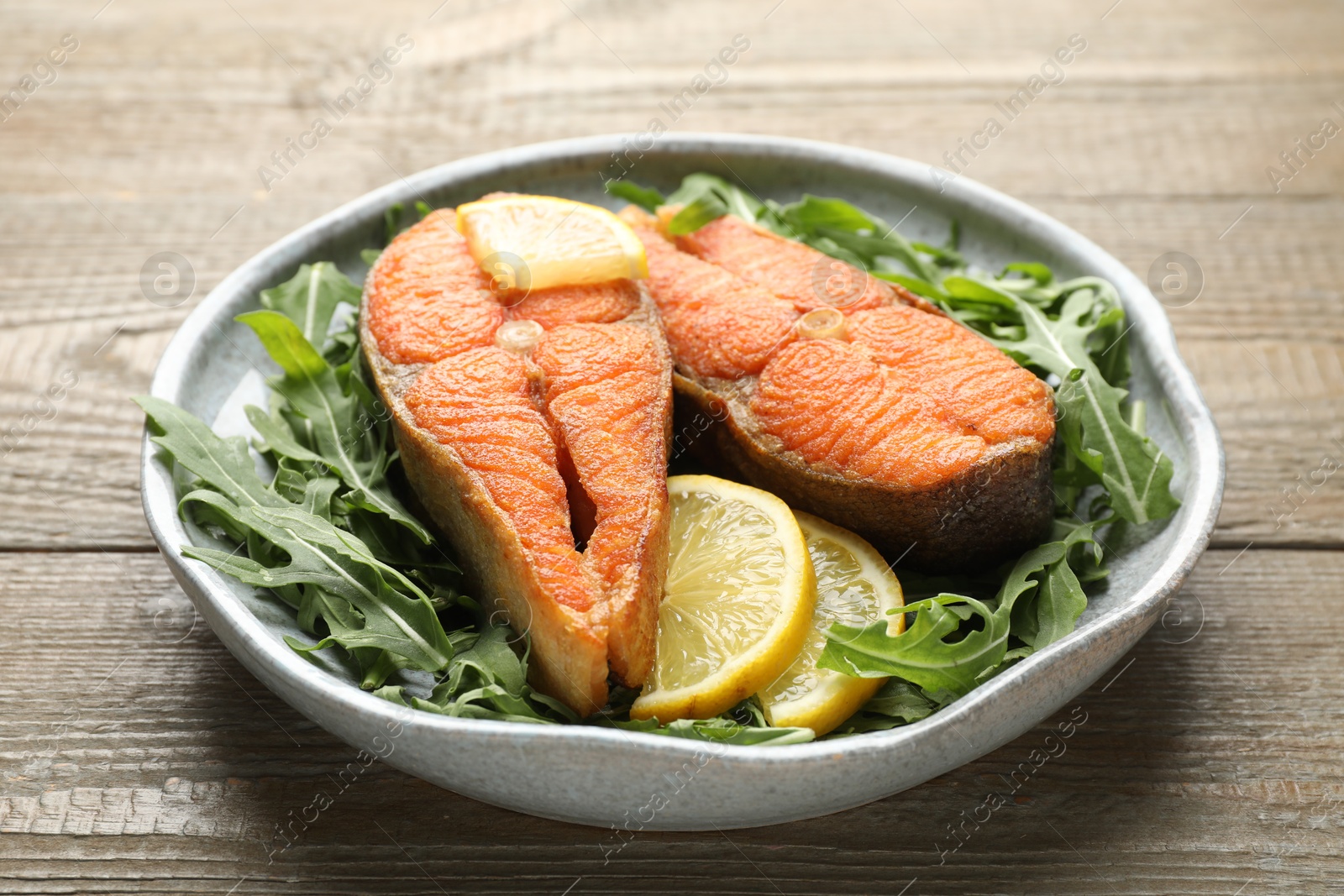 Seafood. Tasty salmon steaks, arugula and lemon on wooden table, closeup Photo of Seafood. Tasty salmon steaks, arugula and lemon on wooden table, closeup