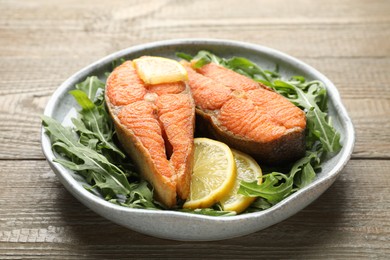 Photo of Seafood. Tasty salmon steaks, arugula and lemon on wooden table, closeup