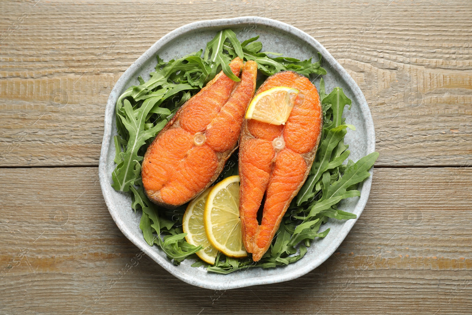 Seafood. Tasty salmon steaks, arugula and lemon on wooden table, top view Photo of Seafood. Tasty salmon steaks, arugula and lemon on wooden table, top view