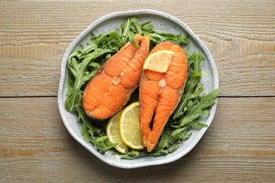 Photo of Seafood. Tasty salmon steaks, arugula and lemon on wooden table, top view