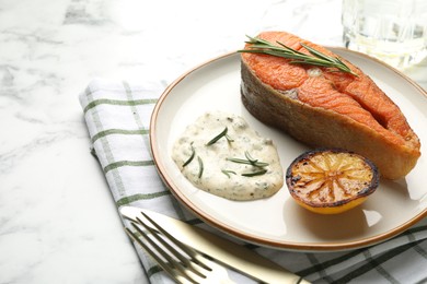 Photo of Seafood. Tasty salmon steak served with sauce, rosemary and lemon on white marble table, closeup. Space for text